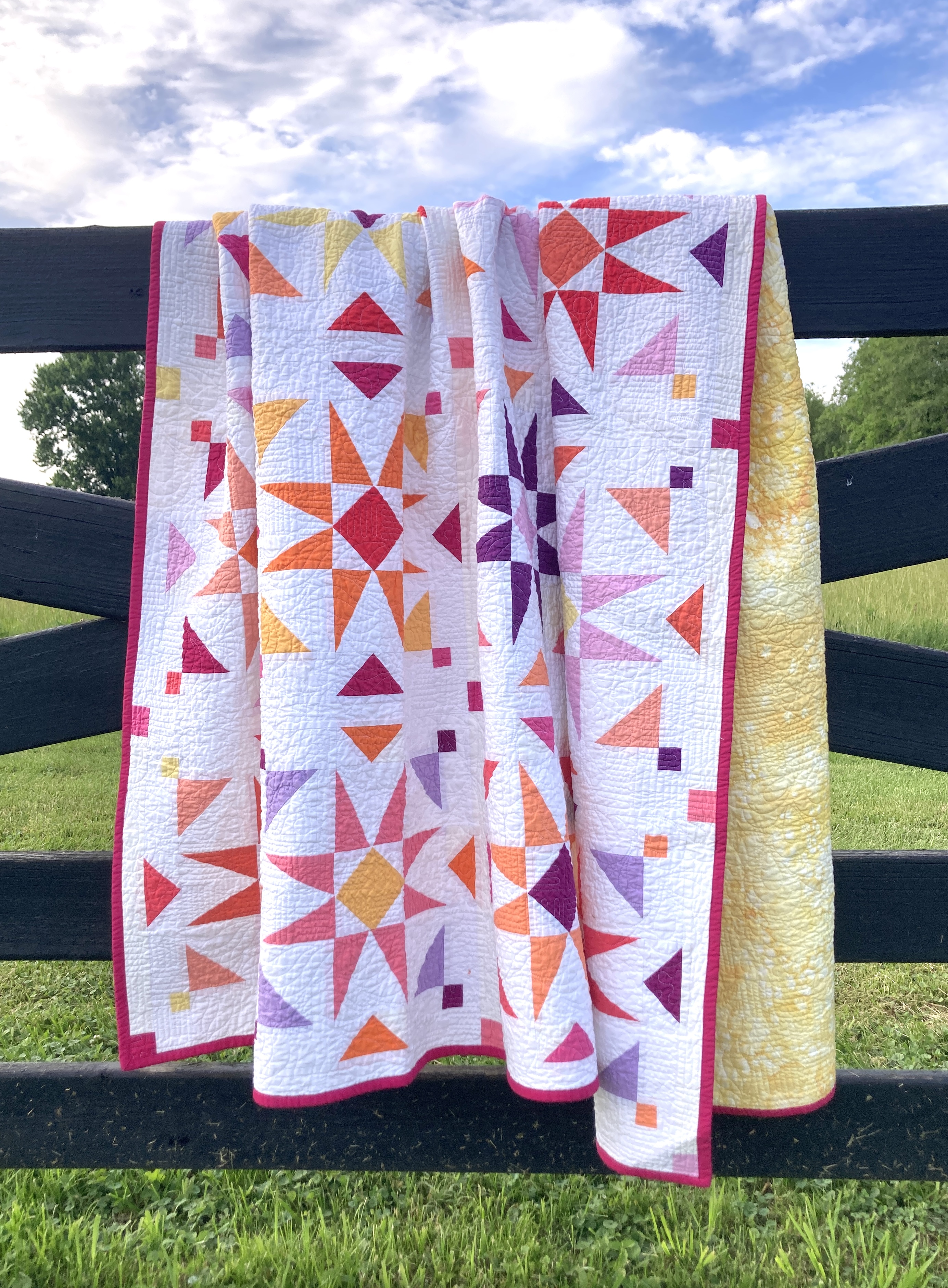 A colorful quilt with scattered starburst blocks hanging on a fence