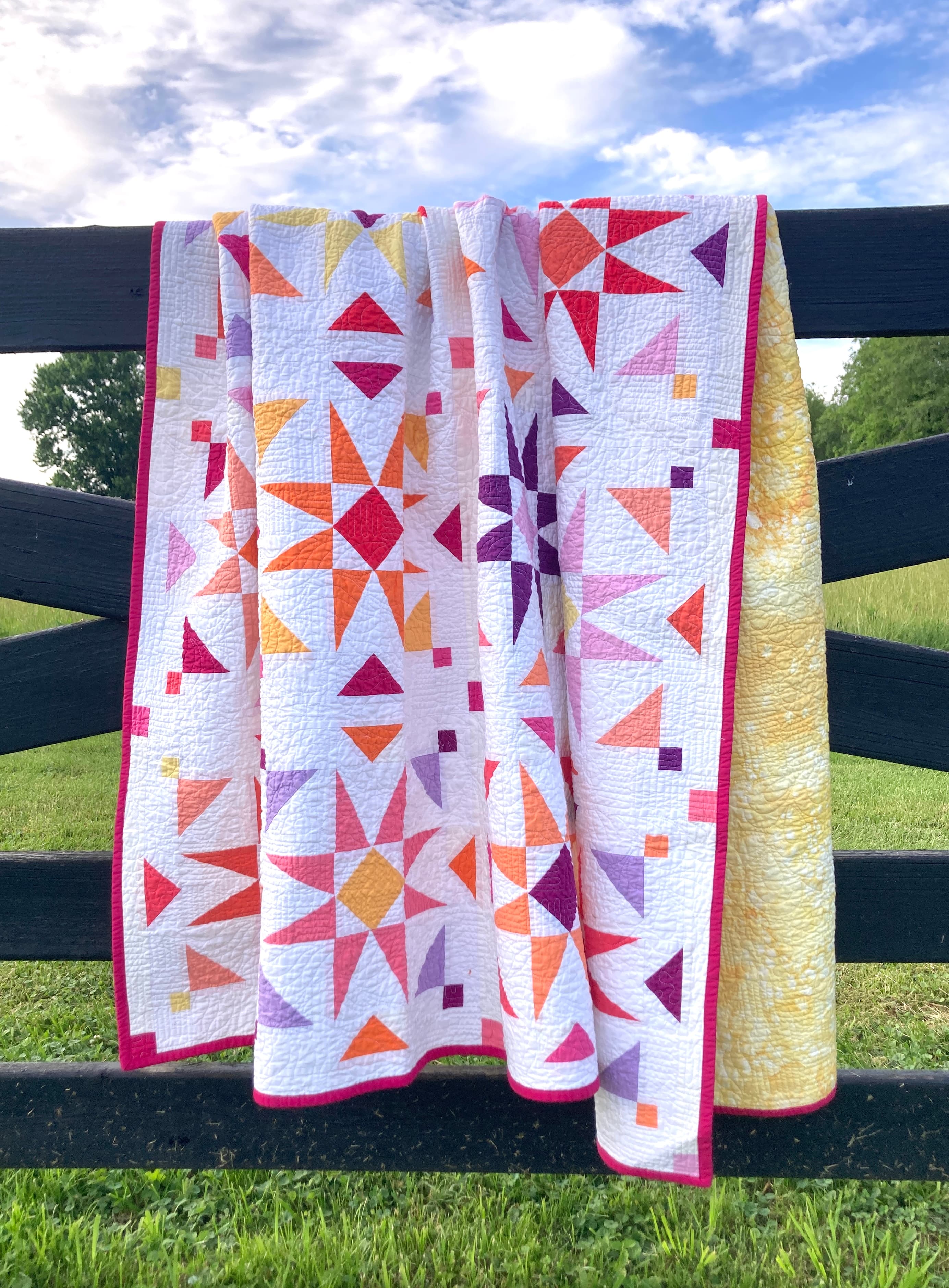 A colorful quilt with scattered starburst blocks hanging on a fence