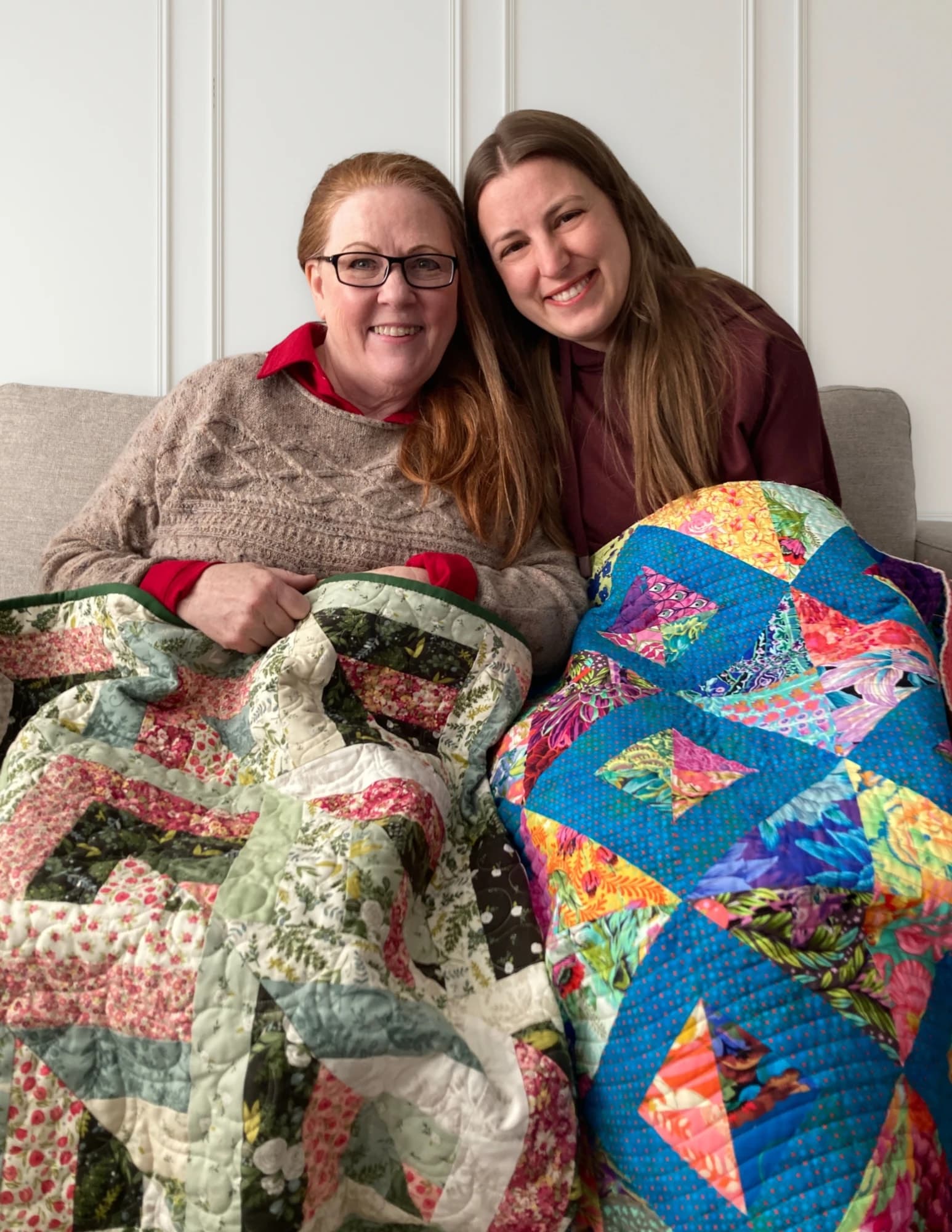 Cheryl and Marsali sitting together, each holding a quilt they made for the other