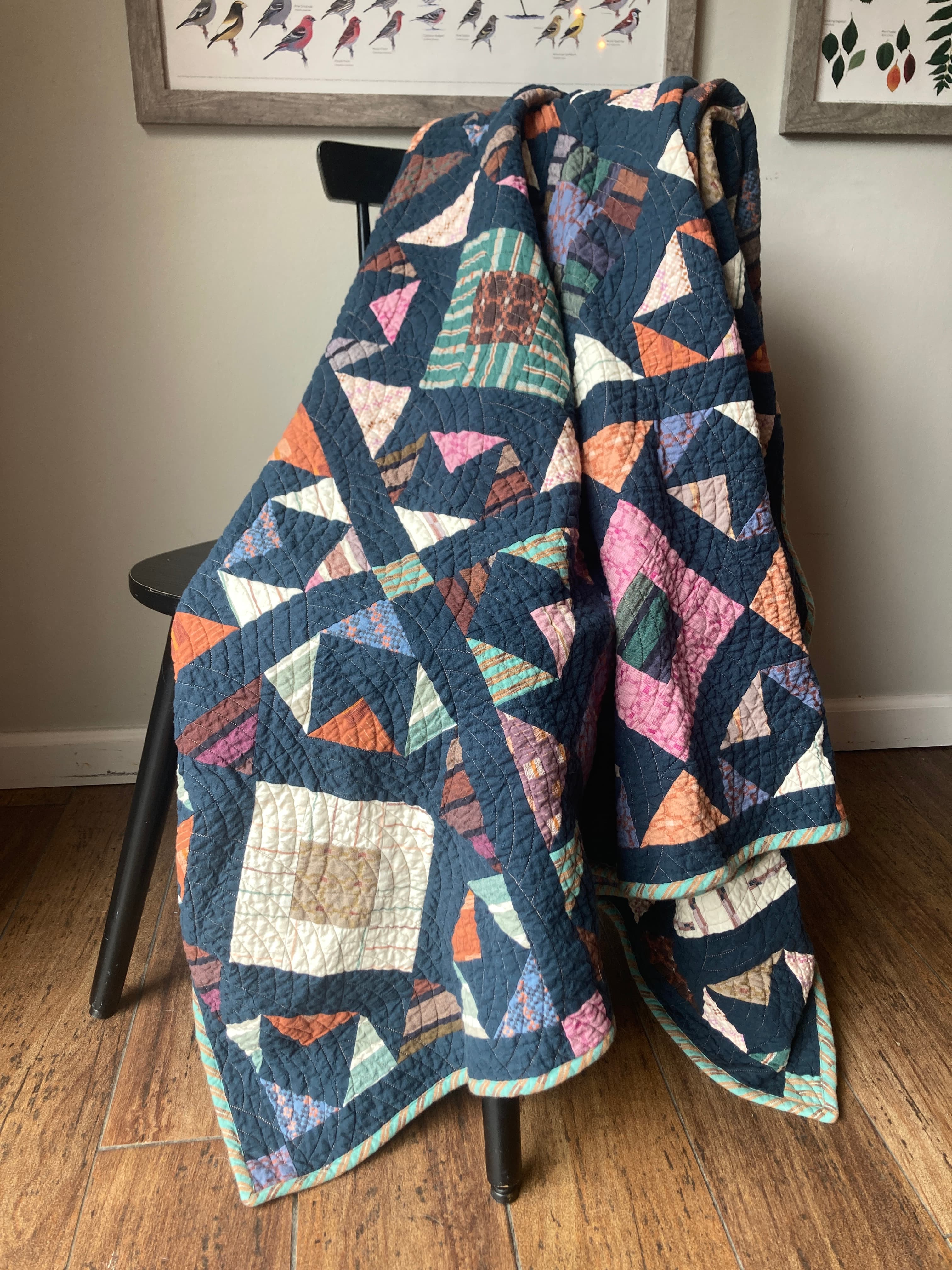 A navy quilt with scattered triangle blocks in woven fabrics, draped over a chair