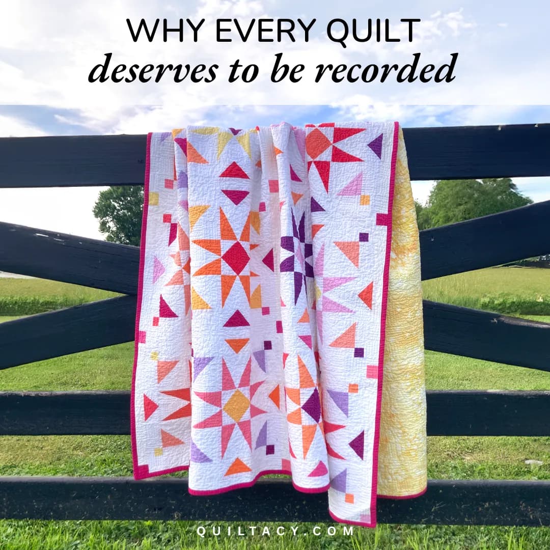 A pink and orange star quilt draped over a wooden fence outdoors